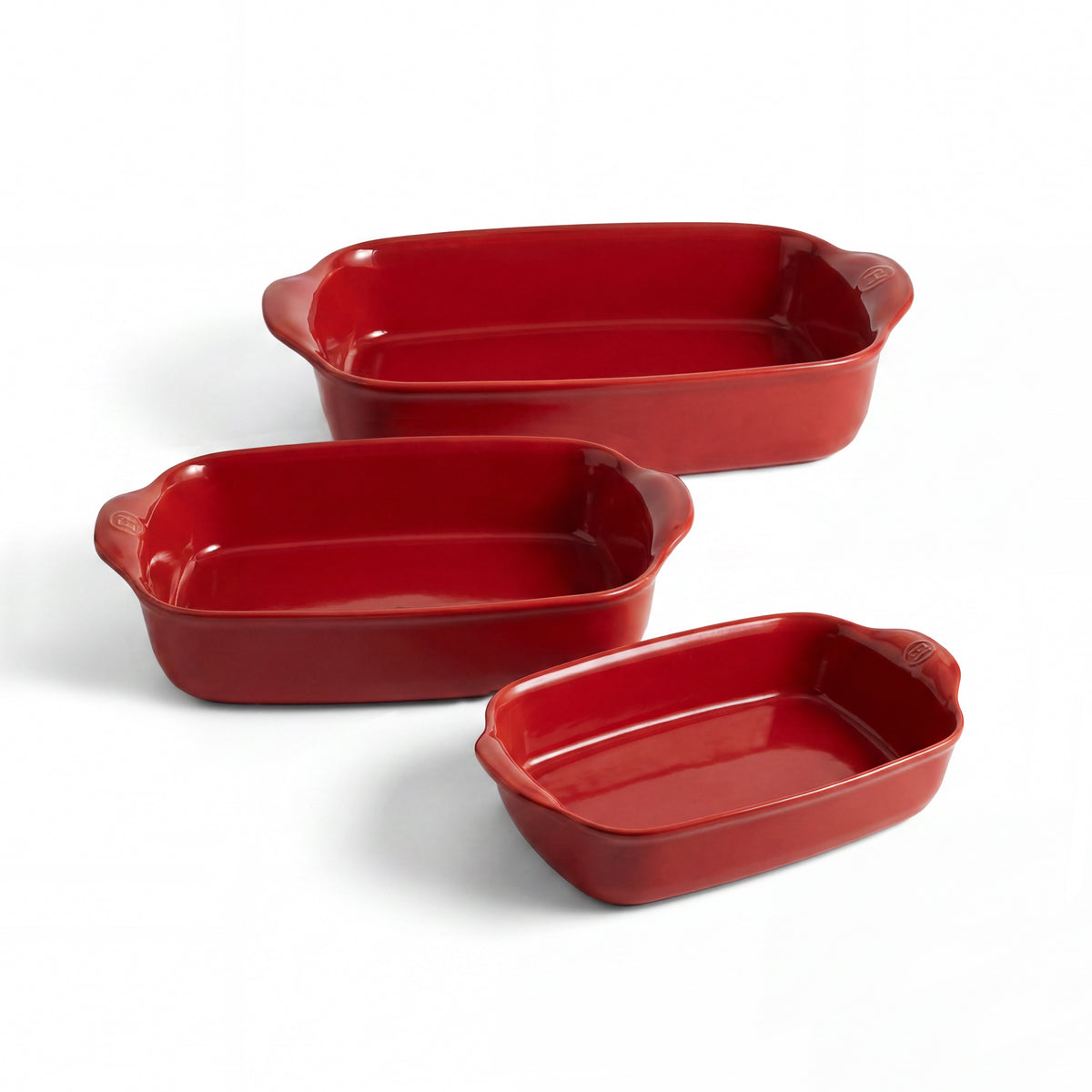Three red rectangular ceramic baking pans in different sizes, arranged diagonally on a clean white background.